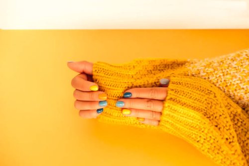 woman in yellow white knitted sweater is demonstrating her hands with bright multi colored manicure above yellow table. trendy colors of the year 2021 - nails art stock pictures, royalty-free photos & images