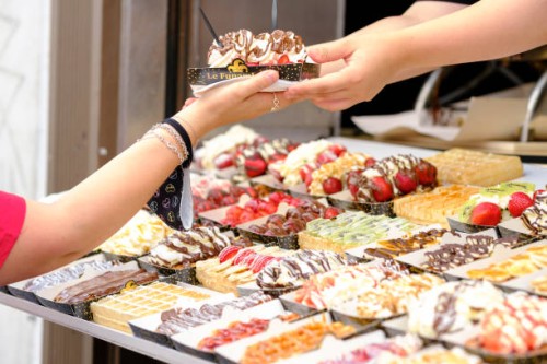 Woman is buying a waffle in a shop on July 29, 2021 in Brussels, Belgium. A waffle is a pastry made with a light dough baked in a waffle iron...