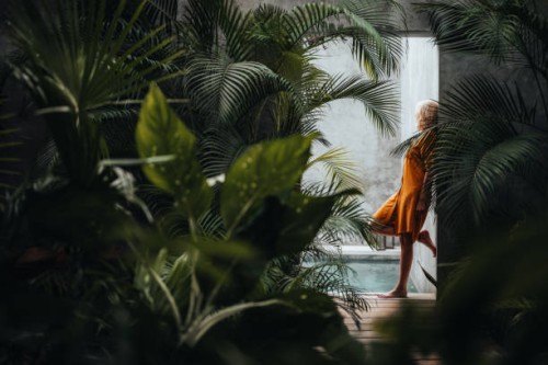 woman leaning on a gray concrete stone wall surrounded by green tropical palm leaves, by the pool. - fashion stock pictures, royalty-free photos & images