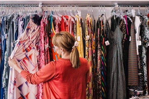 woman looking at dress hanging on rack while standing at store - fashion stock pictures, royalty-free photos & images