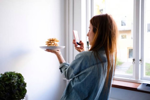 woman photographing waffles through smart phone in plate by wall at home - food stock pictures, royalty-free photos & images