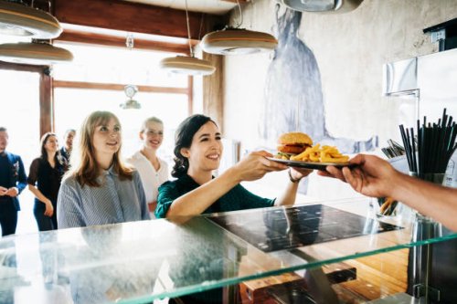woman picking up burger from restaurant counter - junk food stock pictures, royalty-free photos & images