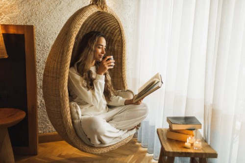 woman relaxing at home in hanging ball chair, reading book and drinking hot herbal tea - home decoration stock pictures, royalty-free photos & images
