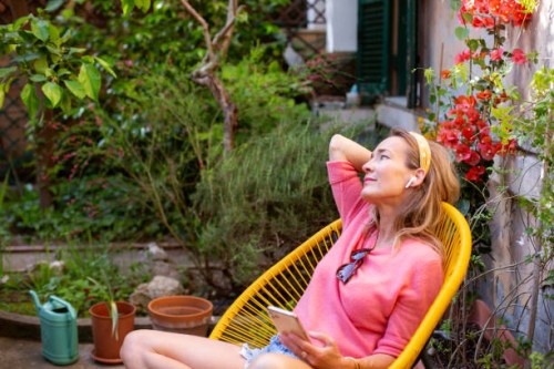 woman relaxing in garden chair, holding smartphone - garden decoration photos et images de collection