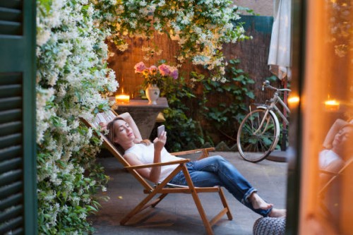 woman relaxing on deck chair in backyard, reading on mobile phone - garden decoration photos et images de collection