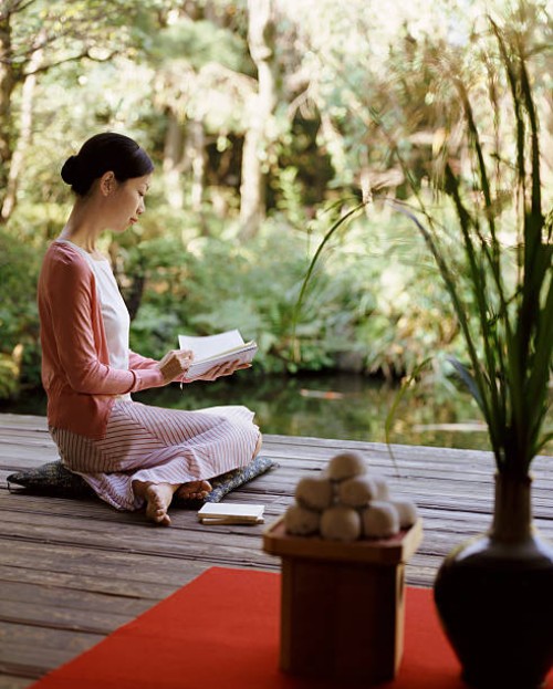 woman sits on a cushion in her garden reading a book - garden decoration stockfoto's en -beelden