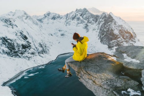 woman sitting on cliff and using smartphone on lofoten island in snow - travel stock pictures, royalty-free photos & images