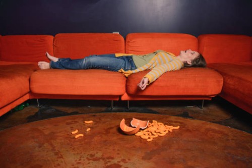 woman sleeping on a sofa and cheese puffs on the floor. - junk food stock pictures, royalty-free photos & images