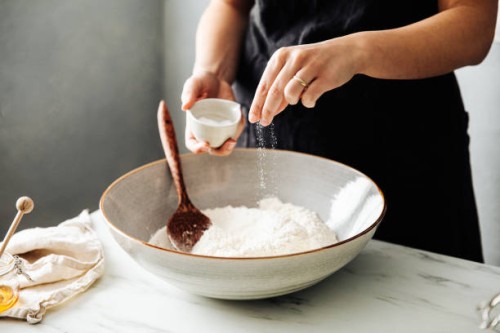 woman sprinkling salt in flour before mixing - food stock pictures, royalty-free photos & images