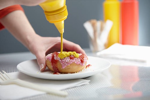 woman squirting donut with ketchup and mustard - food stock pictures, royalty-free photos & images