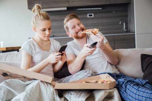 woman text messaging and man eating pizza and holding remote control - junk food stock pictures, royalty-free photos & images