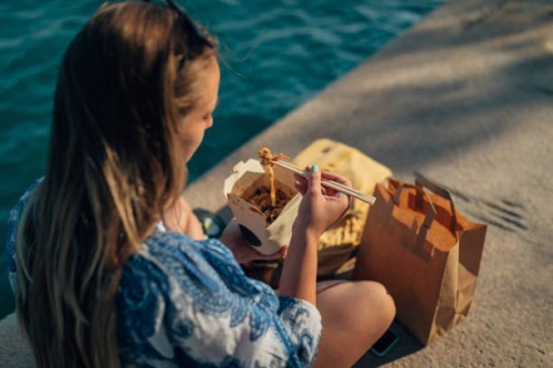 woman uses chopsticks to eat chinese takeout food by the sea - junk food stock pictures, royalty-free photos & images