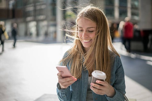 woman walking on the street texting on her phone - junk food stock pictures, royalty-free photos & images