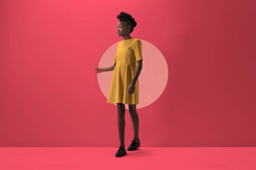 woman walking out from woman peeking out of round opening in coloured wall - fashion stock-fotos und bilder