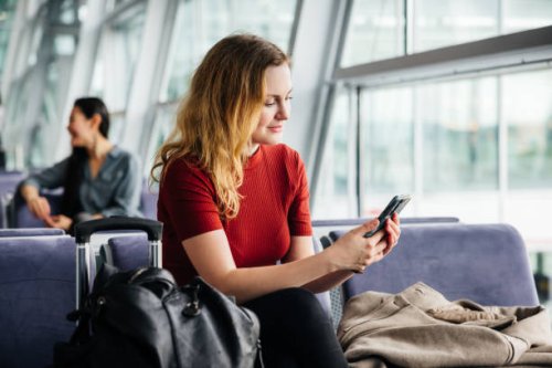 woman wearing red using smartphone while waiting for a flight - travel stock pictures, royalty-free photos & images