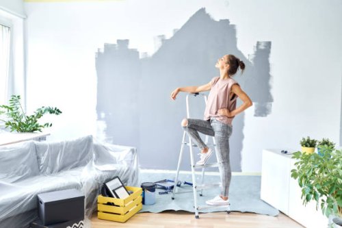 woman with hand on hip leaning on ladder while standing against wall at home - home decoration stock pictures, royalty-free photos & images