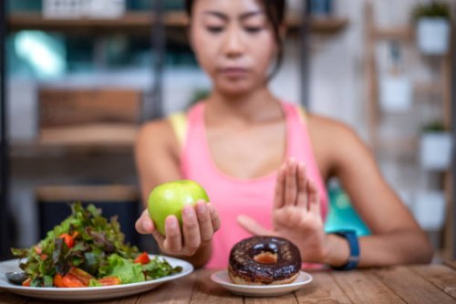 women push the donut plate that is a mixture of trans fat. and choose to hold the apple. don't eat junk food. diet concept - junk food stock pictures, royalty-free photos & images