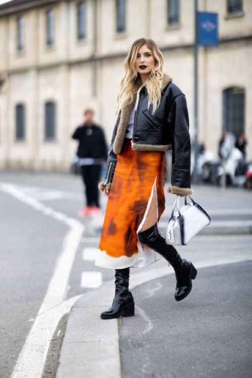 Xenia Adonts is seen wearing an orange printed Prada skirt, black vinyl boots, dark purple lipstick and aviator jacket outside the Prada show during...