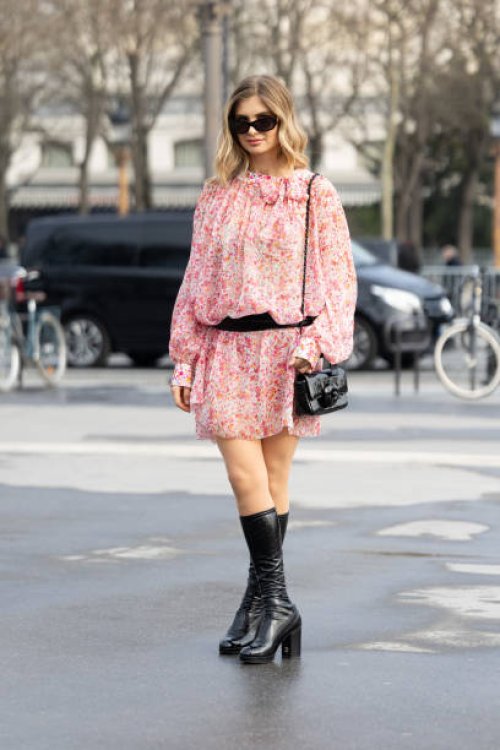 Xenia Adonts wears black sunglasses, a black leather cross-body Chanel bag, a black belt, black knee high leather heeled Chanel boots and a ruffles...