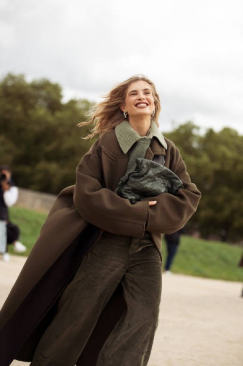 Xenia Adonts wears olive green pants, green sweater, green shirt and dark green oversized coat outside the Loewe show during Womenswear Spring/Summer...