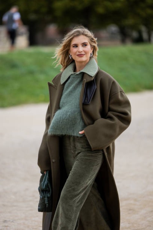 Xenia Adonts wears two tone green brown coat, jumper, corduroy pants, green bag outside Loewe during Womenswear Spring/Summer 2025 as part of Paris...