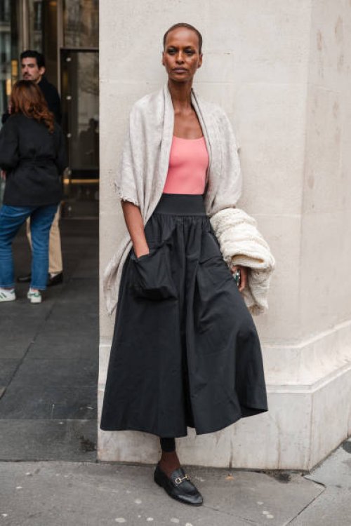 Yasmin Warsame wears pink top, beige scarf on the shoulders, black maxi skirt, black Gucci loafers, outside The Row, during the Womenswear...