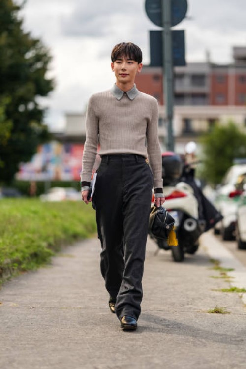 Yoshiaki wears light gray collar light brown gray long sleeve shirt, black high waisted pants, black leather bag with yellow bar charm, shiny black...