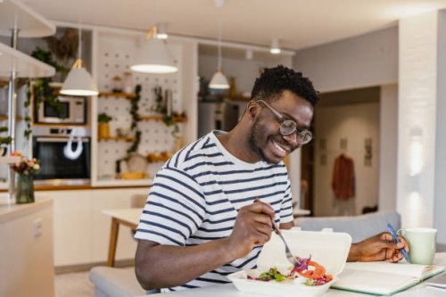 young african-american man eating takeaway meal at home and planning activities - junk food stock pictures, royalty-free photos & images