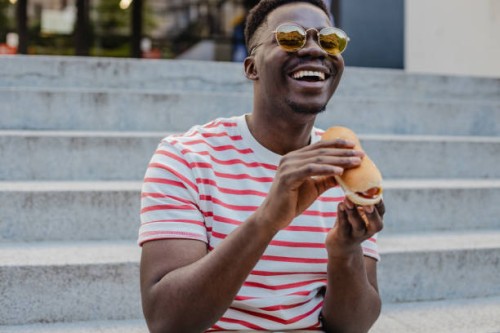 young african-american man is eating hot dog and smiling - junk food stock pictures, royalty-free photos & images