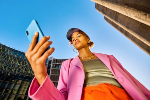 young african american woman in colorful clothing using a smartphone. low angle shot with concrete silos in the background. urban fashion and technology concept. - fashion stock pictures, royalty-free photos & images