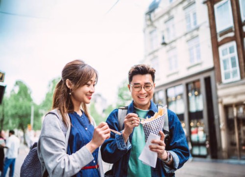 young asian couple enjoying street food together while exploring in vibrant streets of a new city - food stock pictures, royalty-free photos & images