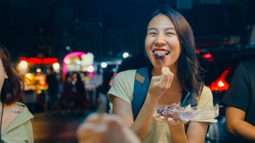 young asian female friends backpacker enjoy eating street food on the street at night market in bangkok, thailand. holiday vacation trip. - food stock pictures, royalty-free photos & images