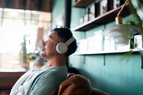 young asian man with eyes closed, enjoying music over headphones while relaxing on the sofa at home - home decoration stock pictures, royalty-free photos & images