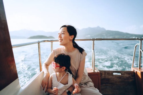 young asian mother and lovely little daughter with red sunglasses enjoying a yacht ride over nice calm sea on a summer day. looking over and relaxed at the sea. family lifestyle. enjoying outdoor fun, boat trip and sea vacati