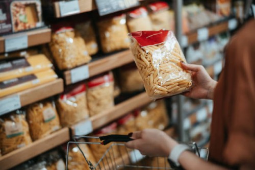 young asian woman carrying a shopping basket, grocery shopping in supermarket, close up of her hand choosing a pack of organic pasta along the aisle. healthy eating lifestyle - food stock pictures, royalty-free photos & image