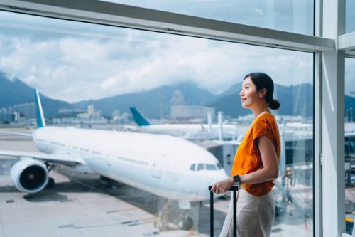 young asian woman carrying suitcase, looking through window at airport terminal while waiting for departure. ready for a trip. business travel. travel and vacation concept - travel photos et images de collection