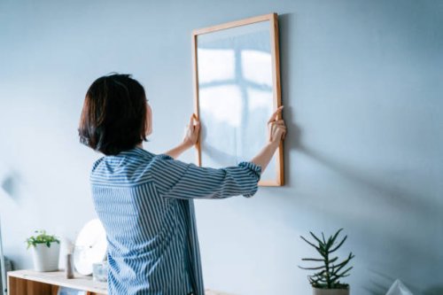 young asian woman decorating and putting up a picture frame on the wall at home - home decoration stock pictures, royalty-free photos & images