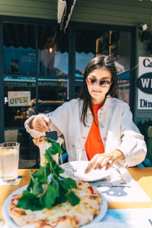 young asian woman holds a piece of pizza in outdoor summer cafe. - junk food stock pictures, royalty-free photos & images