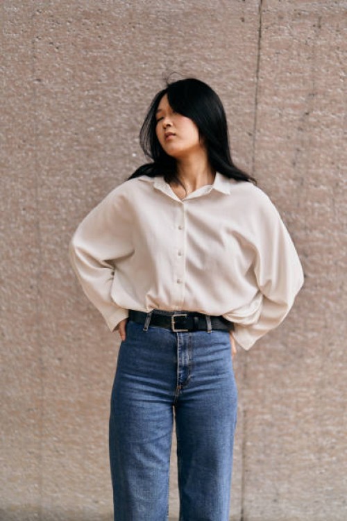 young asian woman posing with hands on hips against concrete wall - fashion stock pictures, royalty-free photos & images