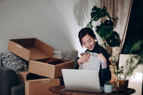young asian woman unboxing new purchase clothings from cardboard box that received from her online shopping retail delivery at home. she is happy and excited to see the content from the box. online shopping, trustworthy parce