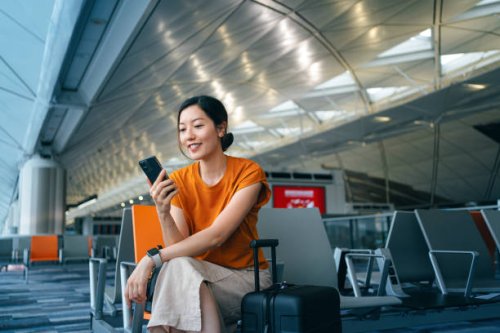 young asian woman with suitcase using smartphone while waiting for her flight at airport terminal. asian businesswoman on business travel. lifestyle and technology. travel and vacation concept - travel stock pictures, royalty
