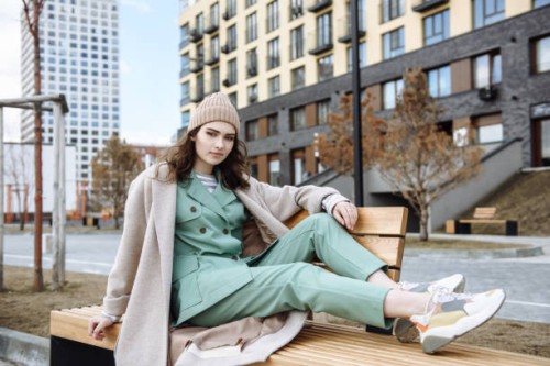 young beautiful teenage girl in a hat and coat sits on a bench and poses against the background of a city street - fashion stock pictures, royalty-free photos & images