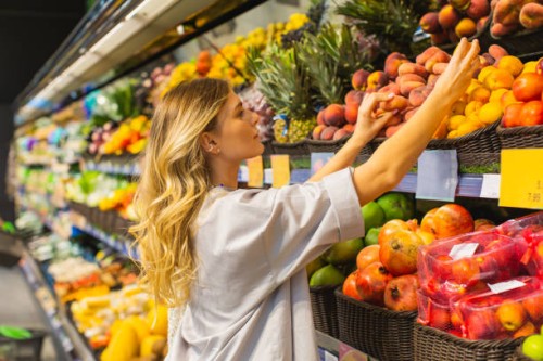 young blonde woman chooses peach in fruit section. autumn market. vegetarianism. healthy food. choice. shopping. select fruits by scent. sniff food - food stock pictures, royalty-free photos & images