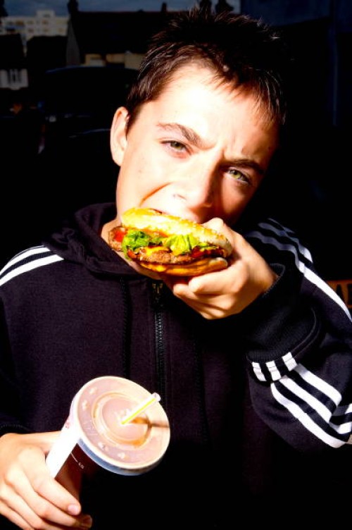 Young boy eating a fast food burger and holding a drink.