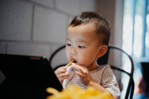 young boy eating and playing digital tablet in cafe - junk food stock pictures, royalty-free photos & images