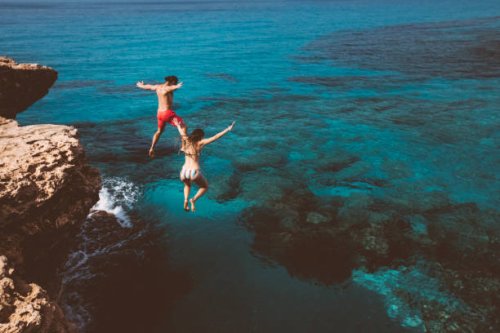 young brave divers couple jumping off cliff into ocean - travel stock pictures, royalty-free photos & images