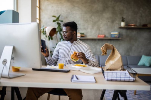 young businessman having a lunch break and eating burgers while telecommuting from home - junk food stock pictures, royalty-free photos & images