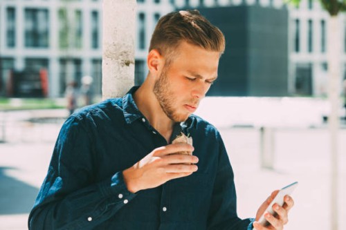 young businessman having lunch outside while looking at his cell phone - junk food stock pictures, royalty-free photos & images