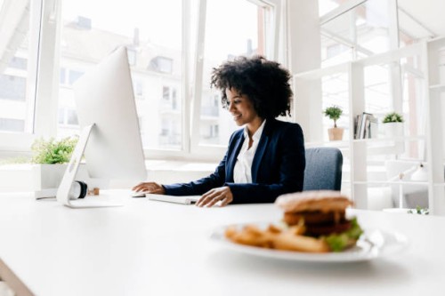 young businesswoman working with hamburger on her desk - junk food stock pictures, royalty-free photos & images