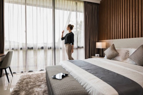 young caucasian woman at home, looking out of modern bedroom window - home decoration stockfoto's en -beelden